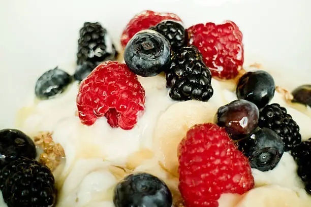 details of a muesli breakfast with redberries some raspberries blackberries blueberries banana with honey and milk and yogurt