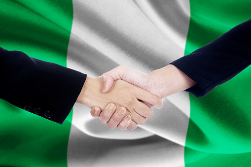 Image of a partnership handshake with two worker hands, closing a deal by shaking hands with Nigerian flag background