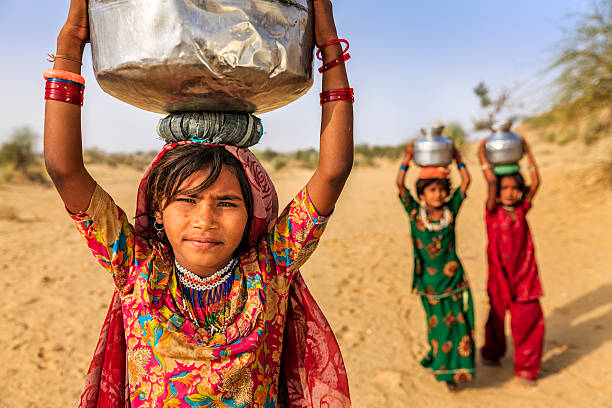 Indian little girls carrying on their heads water from well Indian little girls crossing sand dunes and carrying on their heads water from local well, Thar Desert, Rajasthan, India. Rajasthani women and children often walk long distances through the desert to bring back jugs of water that they carry on their heads.  child labor stock pictures, royalty-free photos & images
