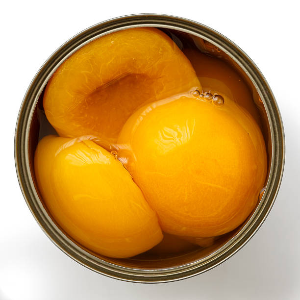 Open can of peach halves in syrup from above. Open can of peach halves in syrup from above. Isolated on white. canned food stock pictures, royalty-free photos & images
