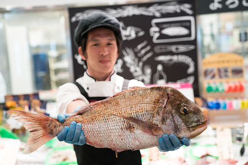 A shop clerk holding up a fresh fish in the supermarket seafood section