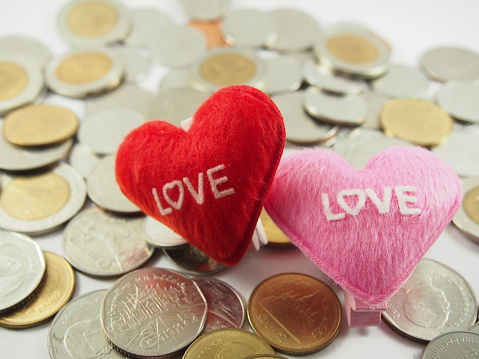 Little pillows with heart shape on pile of coins background (love collected coins, saving money, money for wedding in concept)