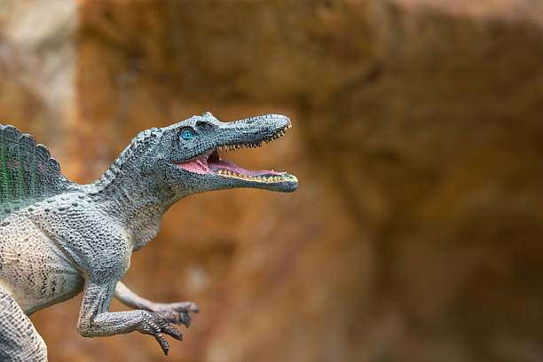 istock grey spinosaurus toy in front of rock mountain 539844546