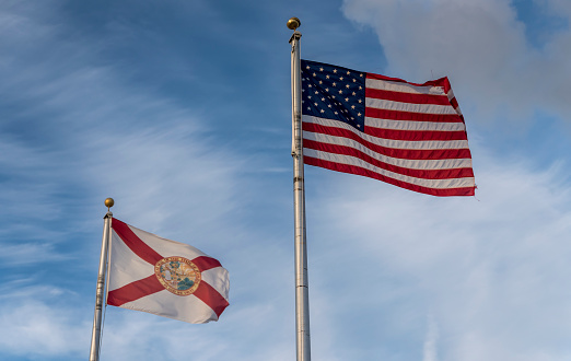 the American and Florida State flag, flying against a blue sky