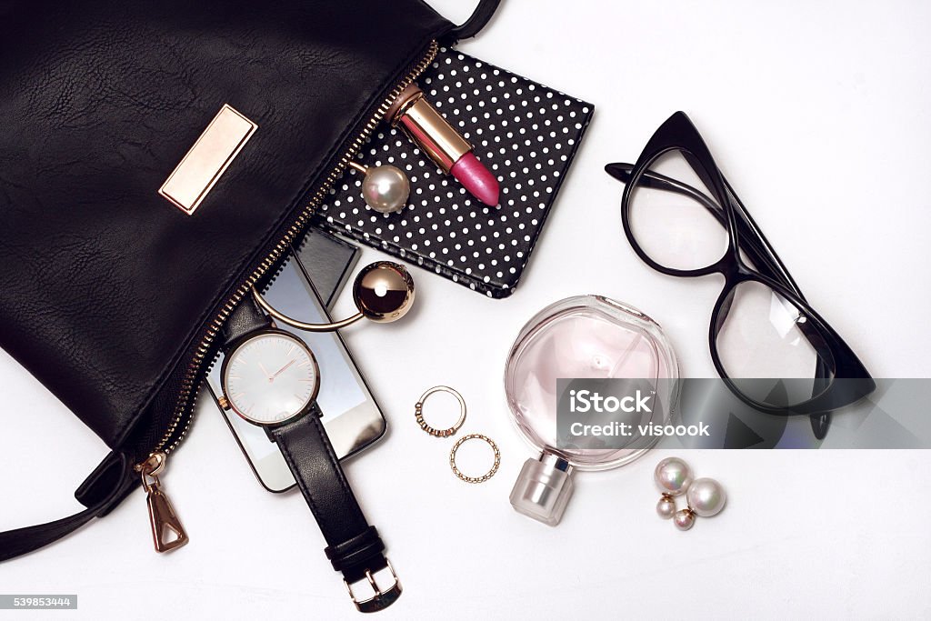 Fashionable female accessories in black bag. Top view Fashionable female accessories watch glasses lipstick perfume and black bag. Overhead of essentials for modern young woman. Personal Accessory Stock Photo