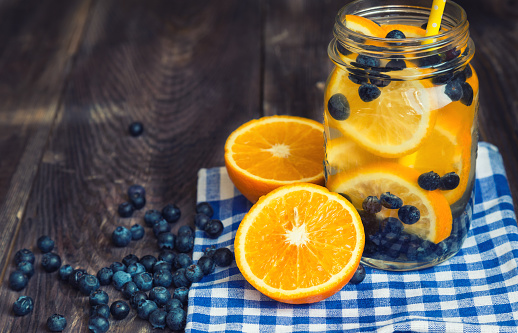 Detox water with orange and blueberries in jar on rustic wooden background.