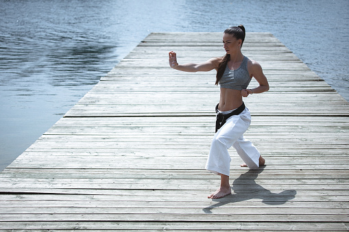 Young woman practising karate on the waterfront. Full length, front view, copy space has been left. Part of the series.