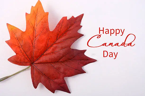 Happy Canada Day symbolic maple leaf on a white wood table with copy space and sample text.