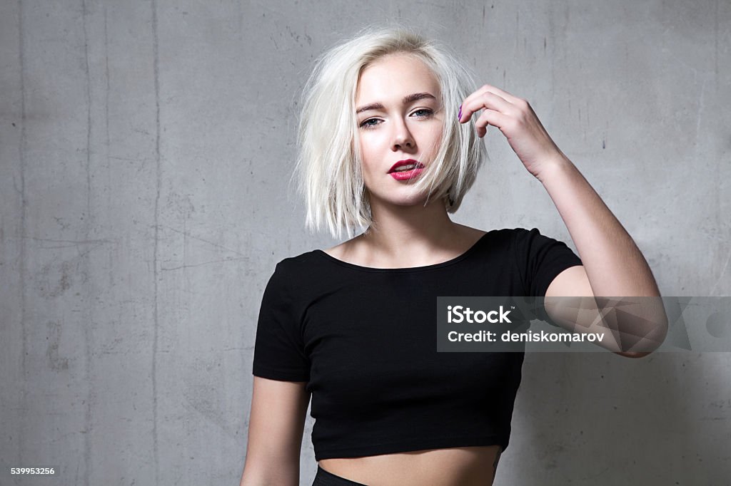 Fashion blonde with short hair and wearing a black T-shirt Portrait of a fashion blonde with short hair and wearing a black T-shirt on the background of a cement wall Bobbed Hair Stock Photo
