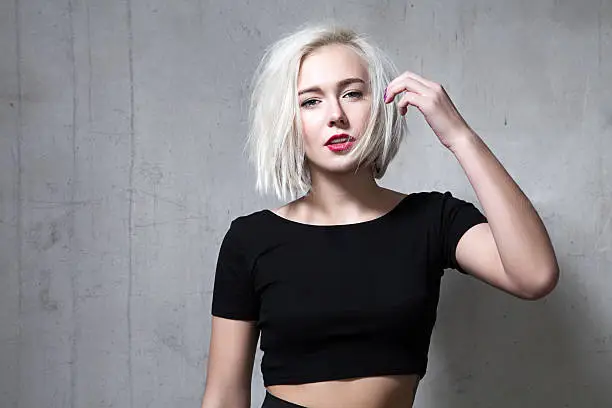 Portrait of a fashion blonde with short hair and wearing a black T-shirt on the background of a cement wall
