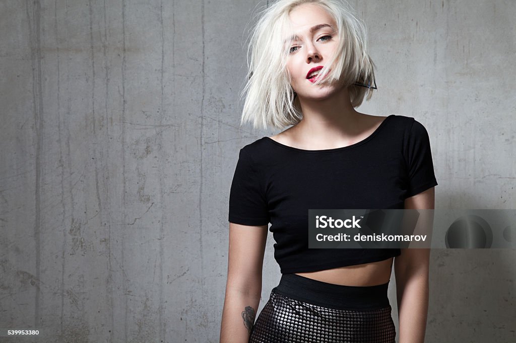 Girl with red lipstick and short hair in  black T-shirt Fashionable girl with red lipstick and short hair and dressed in a black T-shirt, standing on the cement wall background Women Stock Photo
