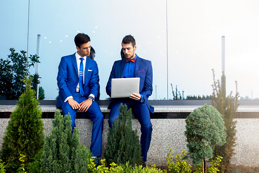 Young businessman and his colleague looking at something on laptop and working outdoors.