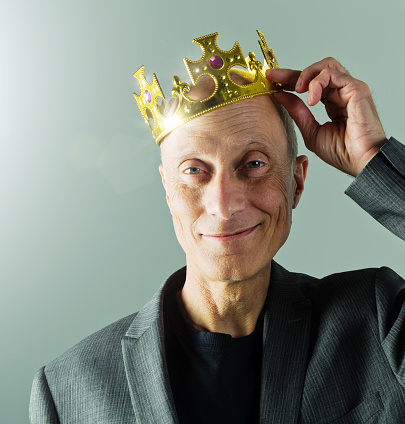 A  smiling senior businessman wearing a golden crown, obviously a leader in his field and happy about it!