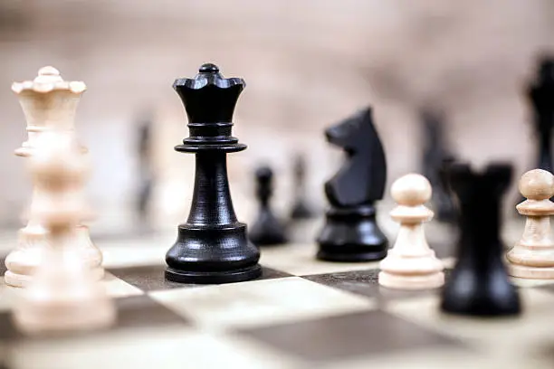 Chess game.  Various chess pieces form a strategic move on a beige and black chess board.  A black king is focal point.  No people.  Strategy concept.