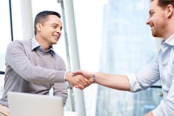 caucasian businesspeople shaking hands in office two caucasian businesspeople smiling and shaking hands in office. day 1 stock pictures, royalty-free photos & images