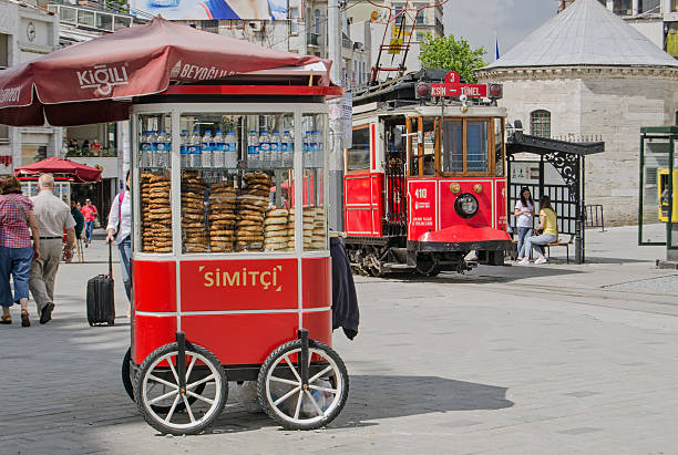 Simit Cart and Tram at Taksim Square, Istanbul Istanbul, Turkey - June 5, 2016:  The nostalgic tram pulling up beside a cart selling traditional Turkish simit bread at the Taksim Square end of the famous Istiklal Caddesi street.  Tourists and locals enjoy the sunshine on a summer morning. turkish bagel simit stock pictures, royalty-free photos & images