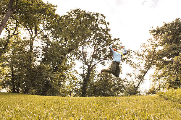istock Successful businessman jumping in the park with raised arms. 539971942