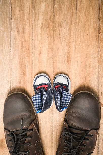 Daddy's boots and baby's sneakers, on wood background, fathers day concept.