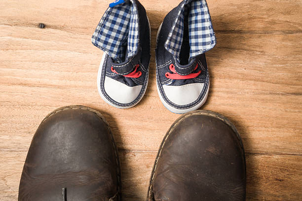 istock Daddy's boots and baby's sneakers, on wood background, fathers d 539975332
