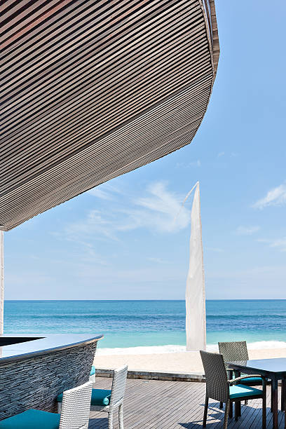 Outside hotel area at sea, water side with blue sky and horizon with dark grey wooden floor and chairs