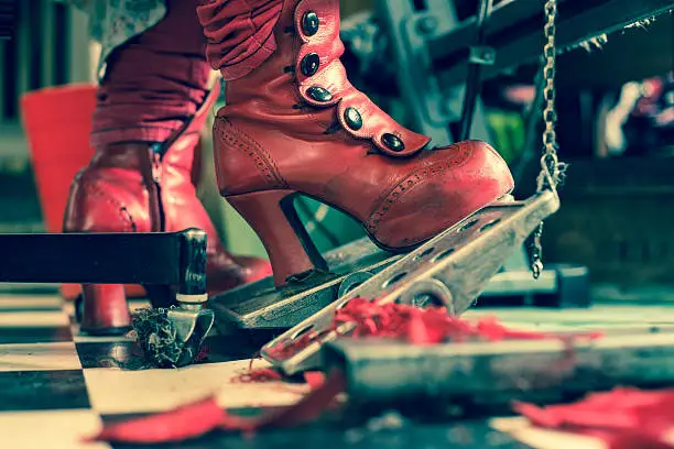 Red fashion boots of seamstress controlling foot pedal of a sewing machine.