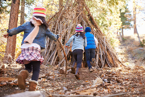 Three kids play outside shelter made of branches in