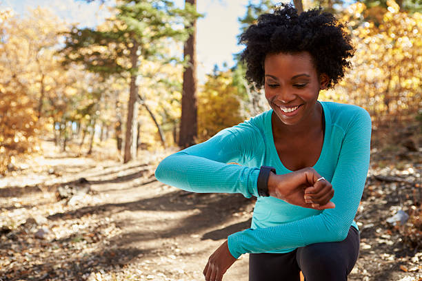 giovane donna in una foresta nera controlla smartwatch e sorridente - running jogging african descent nature foto e immagini stock