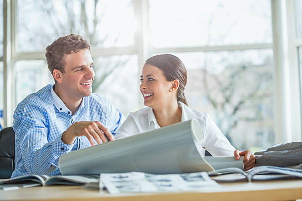 Smiling young architects discussing over blueprint at office desk