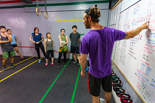 A cross training fitness coach gives instructions to the workout class while the athletes listen in