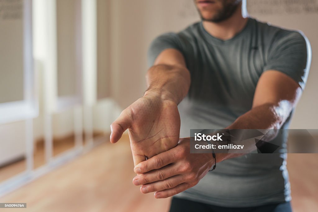 Sporty man stretching forearm before gym workout Sporty man stretching forearm before gym workout. Fitness strong male athlete standing indoor warming up. Stretching Stock Photo