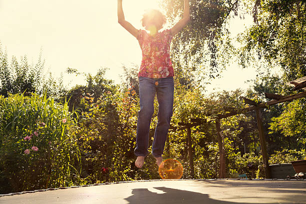 cheerful senior woman having fun jumping on trampoline, outdoors in summer