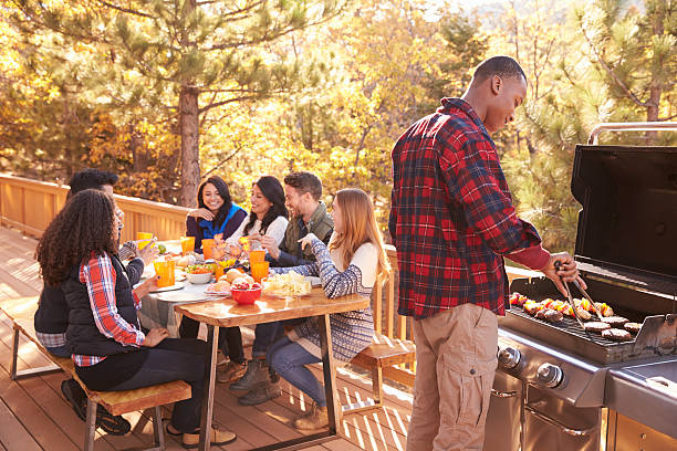 Man barbecues for friends at a table, on a deck in Man barbecues for friends at a table, on a deck in a forest deck stock pictures, royalty-free photos & images