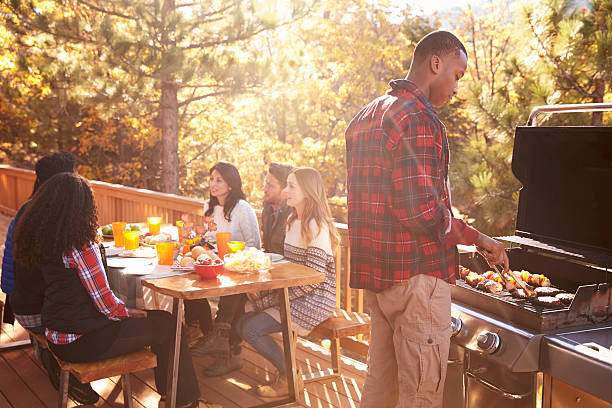 istock Man barbecues for friends at a table on a deck in 540095886