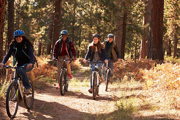 Group four friends in helmets riding bikes on a forest Group four friends in helmets riding bikes on a forest path mountain biking stock pictures, royalty-free photos & images