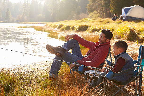 Father and son on a camping trip fishing by a lake Father and son on a camping trip fishing by a lake fishing rod photos stock pictures, royalty-free photos & images