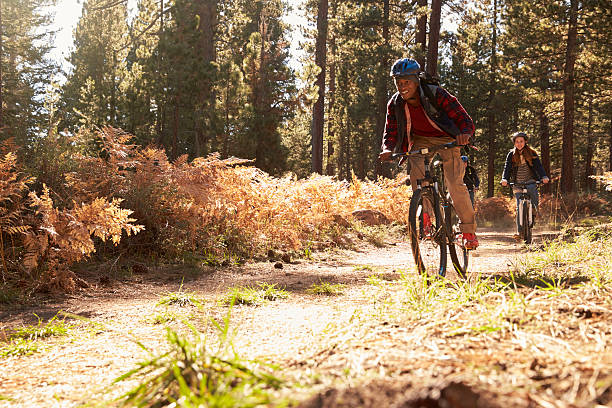 Black man and Caucasian woman riding bikes on a forest Black man and Caucasian woman riding bikes on a forest trail mountain biking stock pictures, royalty-free photos & images