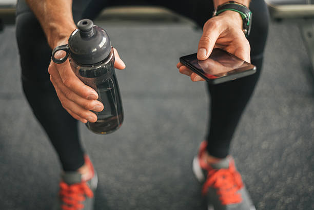 Fitness man looking to the phone for motivation before workout Fitness man looking to the phone for motivation before gym workout. Sporty male athlete looking his smartphone holding water bottle. school gymnasium stock pictures, royalty-free photos & images