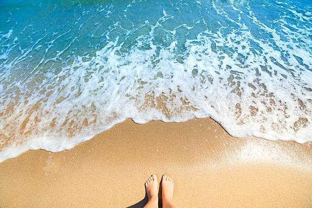 Sea foam, waves and naked feet on a sand beach stock photo