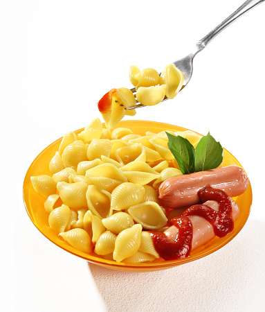 Perfectly cooked macaroni shells skewered on a fork in orange plate on white background. Close up, high resolution product.