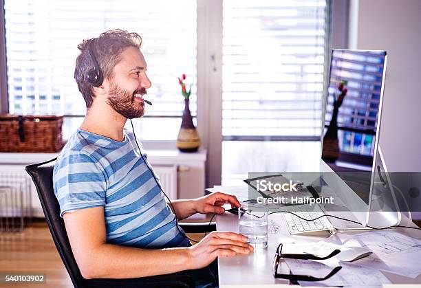 Man Sitting At Desk Working From Home On Computer Stock Photo - Download Image Now - Headset, Computer, Desk