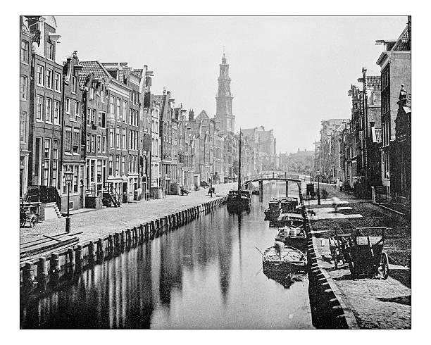 Antique photograph of a Canal in Amsterdam (Netherlands)-19th century Antique photograph of view of a Canal in Amsterdam (Netherlands) as it appeared in the 19th century, with boats, typical houses with their stepped gable façades overlooking the street and the canal, and with the high tower (Westertoren steeple) of the 17th century Renaissance style church called Westerkerk. The 17th-century canals of Amsterdam are on the UNESCO World Heritage List dutch culture photos stock illustrations