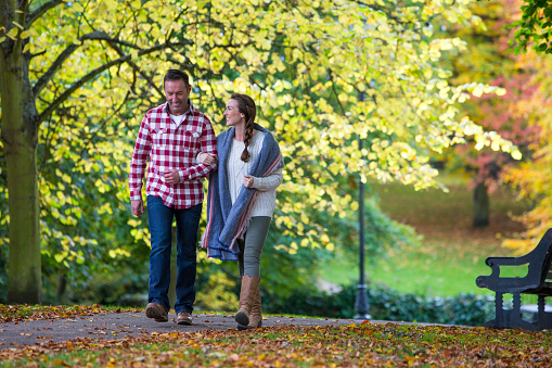 Couple walking through the park during Autumn. They are holding hands and smiling.