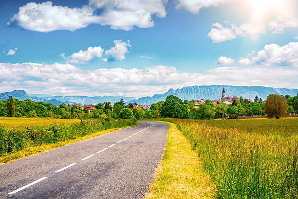 empty countryside road with old french village and alps mountains - landschap dorp stockfoto's en -beelden
