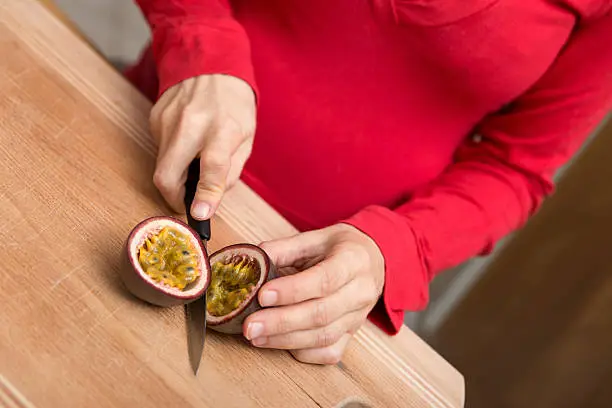 closeup for a pregnant woman is cutting a passion fruit