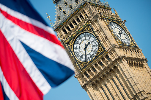 Angled view of the Union Jack flag with Big Ben against a clear blue sky.