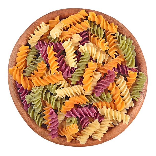 Colored uncooked italian pasta fusilli in a wooden bowl