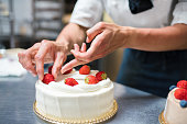 Cake maker placing strawberries on a cake