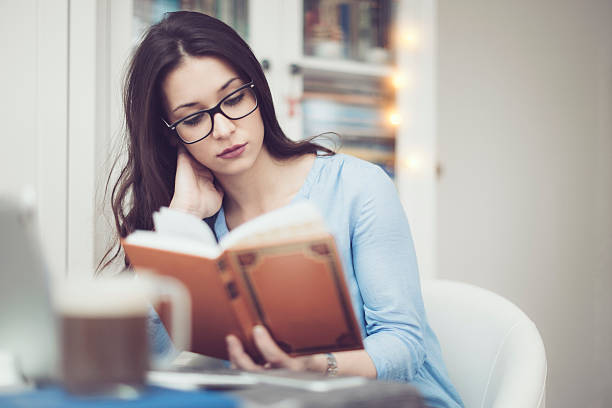 istock Young woman reading a book at home 540122072