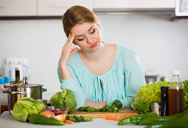 dona de casa jovem cansado de cozinhar legumes na cozinha doméstica - unwillingness imagens e fotografias de stock