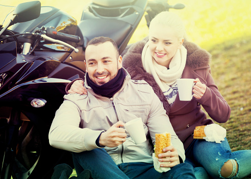 Positive couple having picnic with coffee near cycle